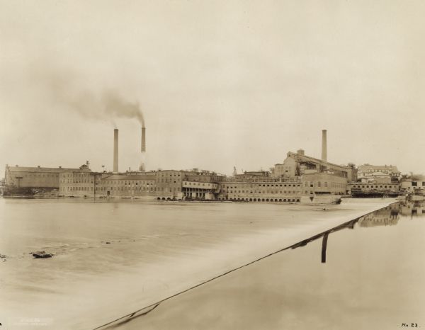 View across water, rushing over a dam, towards the Kimberly Paper Mill.