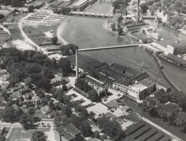 Aerial view of paper mill. There are bridges across the river, including a railroad bridge on the far right.