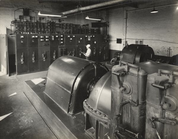 Slightly elevated view across machinery towards an Oscar Mayer employee recording information from equipment gauges mounted on the far wall in the background.