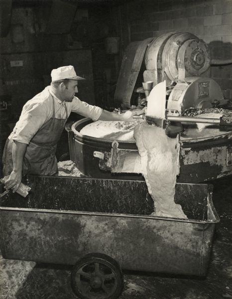 A man is operating the lever of a meat (lard) mixing machine to redirect contents into a wheeled container inside the Oscar Mayer plant.