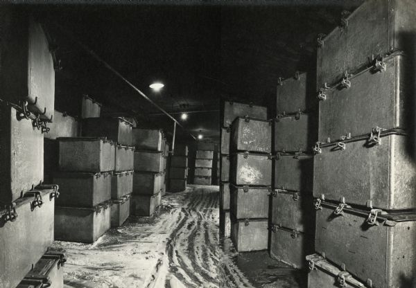 View of a room with rectangular coolers stacked from floor to ceiling. There is a white mixture of greasy and granular contents on the floor between the coolers. The photo seemed to have been stitched together with a vertical line in the middle. 