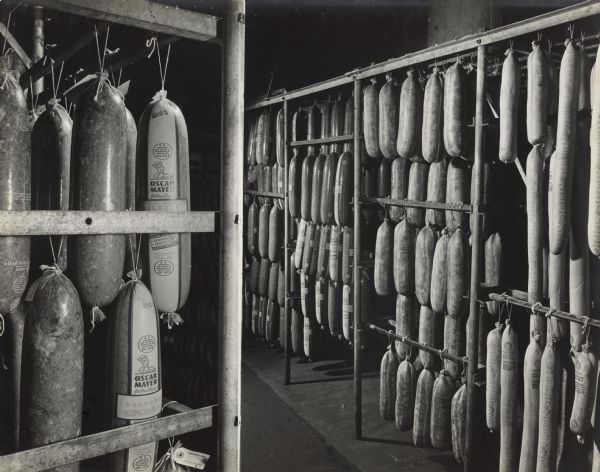 A room with bologna and braunschweiger sausages hanging from racks which are made of a combination of metal frames and wooden cross bars.