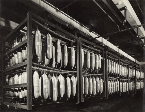View of a large room of packaged Oscar Mayer Cleveland Bologna Sausage. The sausages are hanging from rods on metal frames suspended from the ceiling.