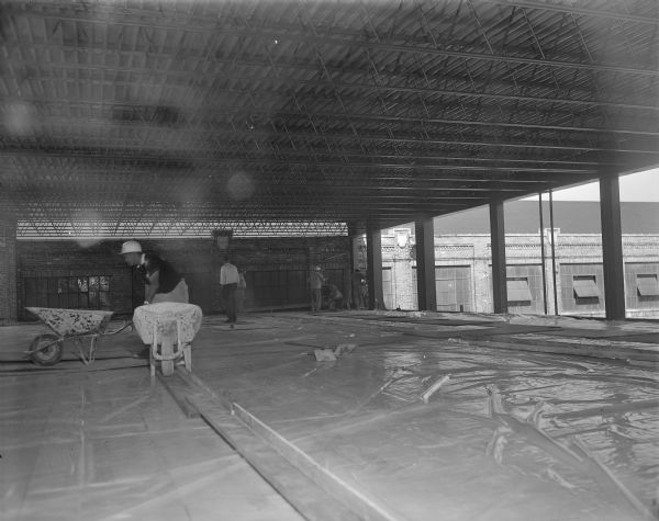 View of workers and supervisors during construction of the skywalk across Baldwin Street at the Gisholt plant. The floor is covered in plastic. The renovation faces East Washington Avenue.