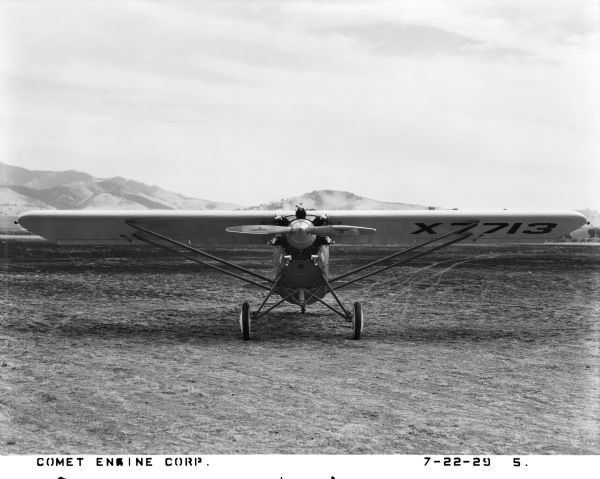 View towards the front of a Sierra BLW-2 aircraft, fitted with a Comet 7-RA air-cooled radial piston engine and a wooden Westinghouse Micarta propeller. Mountains are in the background. The wings and wheels, along with respective struts, are also visible. The 7-RA engine, originally designed by the Comet Engine Corporation in 1928, was manufactured on a Gisholt turret lathe in Madison, Wisconsin, and briefly used on the Sierra line in 1929. Built by Sierra Aircraft Industries which was established in 1928, this BLW-2 was intended for a new aviation school and air-taxi-service based in San Leandro and Modesto, California; the aircraft company ended operations in 1930. The BLW-2 measured 25 ft. 8 in. in length, had a 36 ft. wingspan, and was powered by a 7-RA Comet engine running at 130 hp and 1825 rpm. 

The plane, with registration number X7713, is parked at the Oakland air field. Decal text on the nose reads: "Powered with Comet Aviator Motor." The propeller blades show the Westinghouse manufacturer logo "W" centered in a circle with wings and the words "MICARTA PROPELLER."