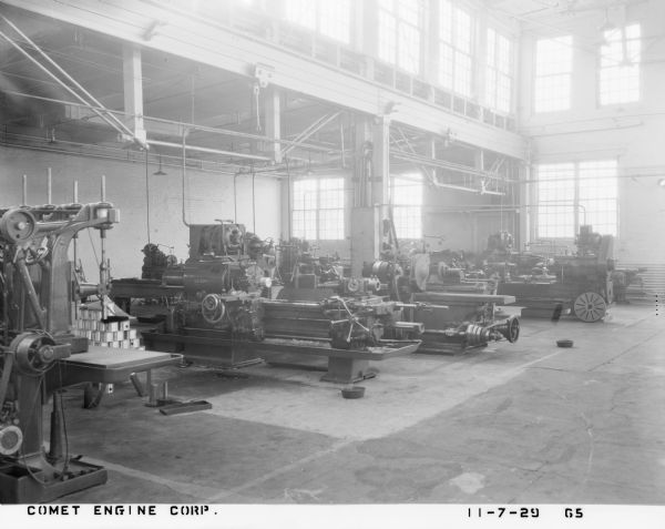 Interior of a factory floor, with several large machines for manufacturing aircraft engines under the skylights. A Gisholt lathe is prominently pictured second from left. Other machinery is by Whitcomb Manufacturing Company, Landis and Cincinnati. 
