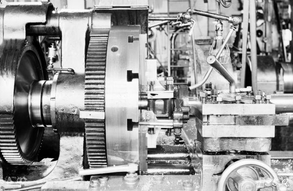 Close-up of a 28" Old Type Gisholt turret lathe at the Packard Motor Car Company factory. This lathe machined a brake band support. 

The original envelope housing this photograph was inscribed with the following information: "Showing special jaws for holding piece, the lower jaw is solid, the upper jaw has a convex bearing between the 4 set screws which are in a plate that is held to the upper jaw with a screw and small spring, the 4 set screws next to the chuck are adjusted and held in position with set screws, the 4 front set screws are adjusted for each piece."