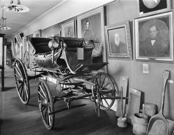 Carriage of Daniel Webster on display at the Wisconsin State Historical Museum, circa 1910-20. Formally displayed at the 1893 World's Fair in Chicago in the Historical Department of the Transportation Building, it remained on loan by Fletcher Webster at the WHS museum for the next twenty-three years, gaining popularity as "easily the most widely known historical relic in the Northwest" (Proceedings of the Society at its Sixty-Fourth Annual Meeting, Held October 19, 1916," 1917, p. 69).

It was originally purchased in London in 1808, by a Bostonian, and then owned of Daniel Webster. According to the museum catalog record, "Martin Van Buren, Henry Clay, Daniel Webster, Silas Wright, Charlotte Cushman, Dean Richmond, Erastus Corning and many other notables of Daniel Webster's day, have ridden in this carriage."