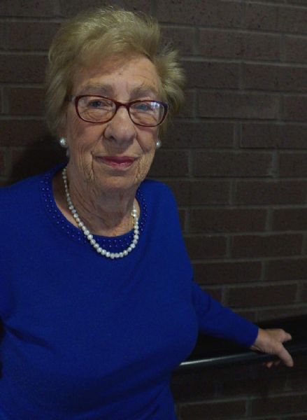 Waist-up portrait of Eva Schloss, a Holocaust survivor, author, playwright, and Anne Frank's step-sister. She is wearing a blue shirt, a pearl necklace and earrings, and eyeglasses.