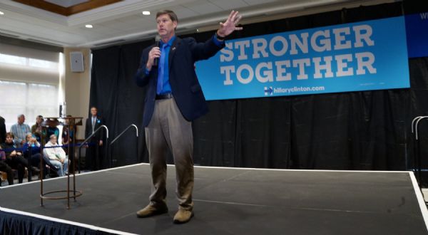Wisconsin's Third District Congressman, Ron Kind, is standing on a stage and speaking into a microphone at a Hillary Clinton rally at UW-La Crosse. A banner reading: "Stronger Together" is hanging behind him.