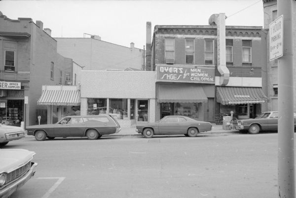 View across West Mifflin Street towards four businesses. From left to right is McDonald's Barber Shop, The Winemaker Shop, Dyer's Shoes, and Paco's Restaurant. Badger Office Supplies is on the far left.
