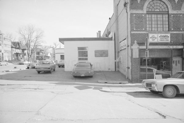 View across North Henry Street towards the Quick Clean Center, on the corner of Gorham Street. Cars are parked in the small lot. On the right is the Plaza Tavern & Grill.