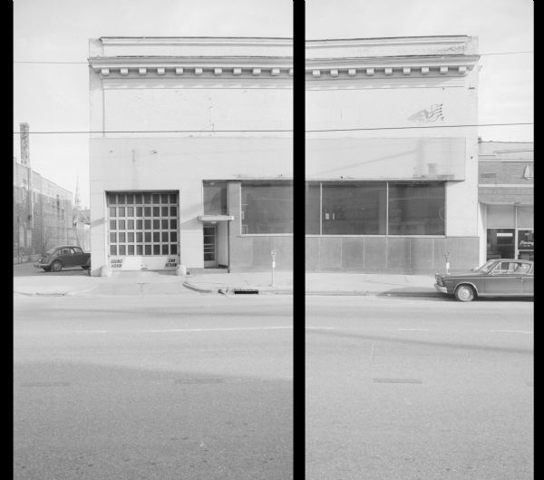 View across West Johnson Street towards Koch Motors, historically the L.A.A.W. Stables. Signs on the bottom of the garage door (on the right) read: "Sound Horn, Car Return." The building on the right is the Guild Printing Company, Inc. The alley on the left separates Koch Motors from Rundell's Beauty Salon. In the background on the left is the steeple of St. Raphael Cathedral, at 222 W. Main Street.