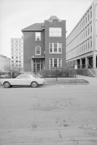 View across East Campus Mall (in 1973 called North Murray Street) towards the Office of Inter-College Programs. A car is parked along the curb at a meter. 