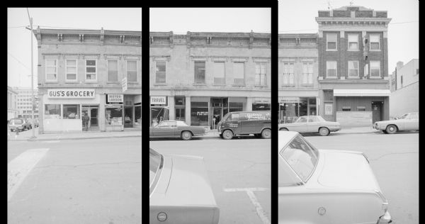 View across South Pinckney Street, on the corner of East Doty Street, at the Van Bergen Block (left) and Albee's Block (right). From left to right, the businesses within the building are: Gus's Grocery, Meyer-Larson Travel, Legal Services Center of Dane County, Kindschi Leather Co., and Hide-A Way (a pub). Cars are parked on both sides of the street, including a van for Badeau Plumbing.