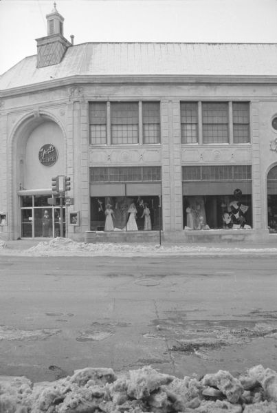 View across State Street, on the corner of North Fairchild Street, towards the Yost-Kessenichs Department Store. The facade of the building is in the Beaux-Arts style. Mannequins in the show windows and entryway are displaying women's clothing, including a wedding dress in the window to the right of the main entrance.