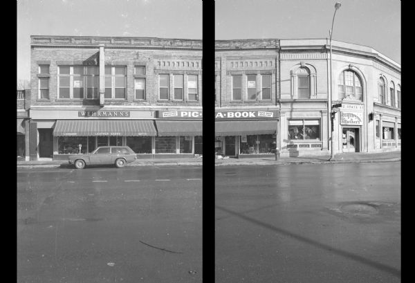 View across State Street, at the intersection with West Gilman Street, towards two buildings. The building on the left is the Hess & Schmitz Building. The ground floor contains two businesses: on the left is Wehrmann's Luggage and Leather Goods, and on the right is Pic-A-Book. Several signs in the second floor are advertising space for rent. The building on the corner is Bigsby & Kruthers, a clothing store.