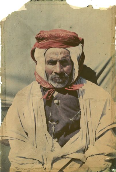 An autochrome waist-up portrait of an Algerian man wearing a turban. He is wearing a western style vest under his robe; a key is hanging from a chain attached to a buttonhole of the vest.