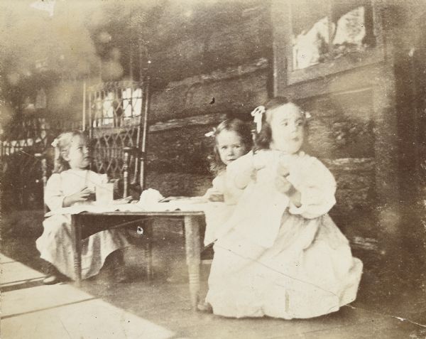 Three cousins are sitting at a table eating a meal on the porch at the Island Lodge on Archibald Lake. Names from left to right are: Harriet Stroh, Margaret Stroh and Jeannette Holt.