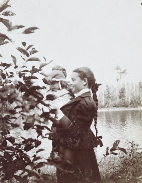 Annie McClure is holding Jeannette Holt while looking at a bird's nest in a tree. Archibald Lake is in the background. Caption reads: "A Birds Nest — Annie McClure."