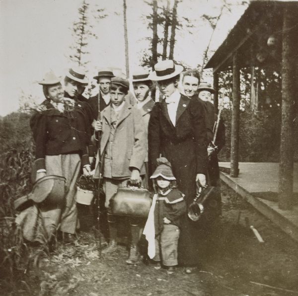 The group of Holts and McClures is departing Island Lodge for home. Names from left to right are: Annie McClure, Jim McClure Jr., Lucy Holt, Jeannette Holt, and Ellen Holt. Caption reads: "Home, Sweet Home — Nit a la Dr. McClure." Caption below reads: "Annie McC., Jim, 'Mai', JRH, Ellen Holt."