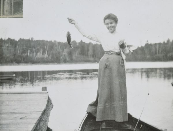 Annie McClure is standing in a boat showing the fish she caught on Archibald Lake. There is a pier on the left, and a tree-lined shore is in the background. Caption reads: "Annie McClure."