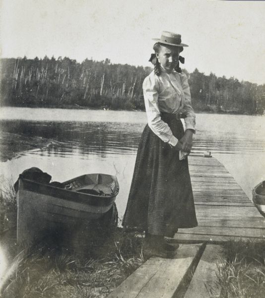 Jeannie Schauers is standing on wooden planks near a pier on the shoreline of Archibald Lake. A rowboat is pulled up on the shoreline on the left.