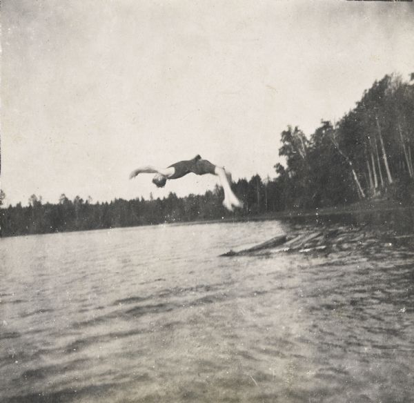 Wallace Donelson Rumsey, the photographer's younger brother, is doing a back flip dive off a raft into Archibald Lake. He was named after Civil War General Wallace and the battle of Fort Donelson. Holt's father Captain I.P. Rumsey served as Assistant Adjutant to General W. H. L. Wallace at Fort Donelson and Shihloh. The natural shoreline of trees and grasses is in the background. 
