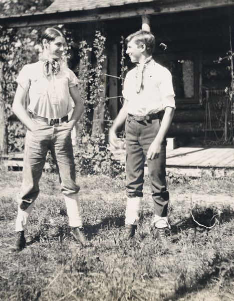 Two young men are standing in front of Island Lodge. They are wearing neck kerchiefs and spats. The young man on the right is James McClure. Caption reads: "Chums." 

