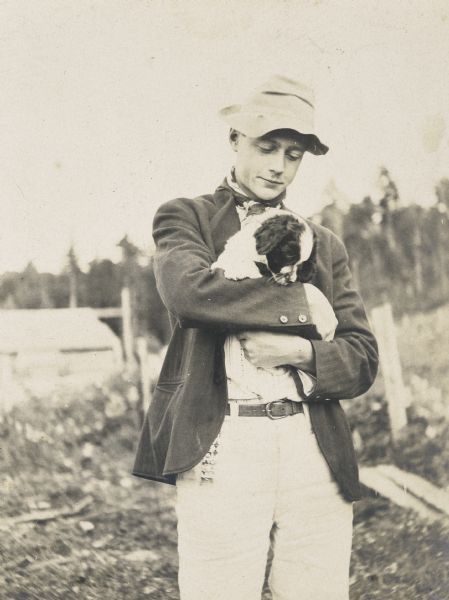 Portrait of a young man holding a puppy in his arms. Trees and a building are in the background. Caption reads: "Horace."