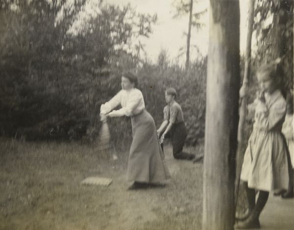 Annie McClure is swinging a baseball bat. Behind Annie a boy is playing catcher. There is a girl, possibly Jeannette Holt, on the right watching the game. Caption reads: "A strenuous effort — Annie at the bat." The caption may be a reference to the poem "Casey at the Bat" by Ernest Lawrence Thayer, published on June 3, 1888.
