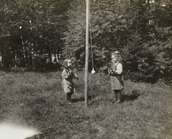Holding lawn tennis rackets, siblings Donald and Eleanor Holt are playing tether ball. The  wooden pole with the tethered ball is standing between the two children. Caption reads: "Donald, Eleanor."