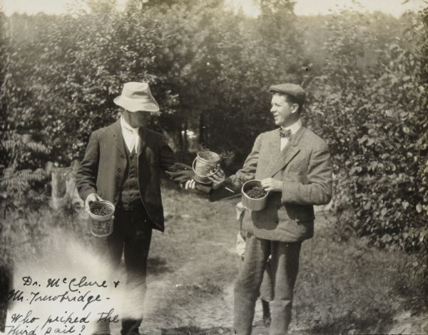 Dr. James McClure, on the left wearing a three-piece suit, and Mr. Trowbridge, on the right wearing a coat and bow tie, are holding pails of freshly-picked berries. They each have their own pail as well as a pail they are both holding. A plant is in the shared pail. Trees are in the background. Caption reads: "Dr. McClure & Mr. Trowbridge — Who picked the third pail?"

