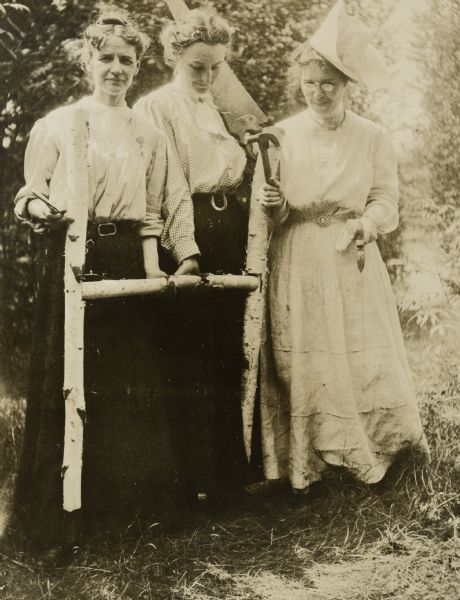 Three wood workers are showing the "H" which they made out of birch logs. From left to right: Lucy Holt, Minnie May Rumsey and possibly Juliet Rumsey Stroh. The "H" stands for Hermit Island where it was later displayed.


