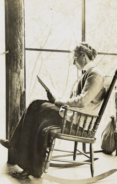 Ellen Holt is reading a book while sitting in a rocking chair on the porch. She is wearing a jacket and skirt. Caption reads: "Ellen Holt."