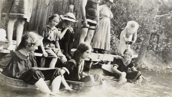 Sitting in galvanized wash tubs with their legs in the water, three girls are ready for the race on Archibald Lake. Jeannette Holt is in the middle, flanked by Margaret and Harriet Stroh. The girls' bathing suits have a sailor collar, and are worn over bloomers.

Sitting on the pier with her feet in the water, Eleanor Holt is watching the racers. Wearing a hat, Minnie Vendt, housekeeper for the Holts in Oconto starting in 1898, is standing on the pier to the right of the man in a bathing suit. The woman to the right of Vendt is holding a camera.  Caption reads: "Minnie Vendt."

