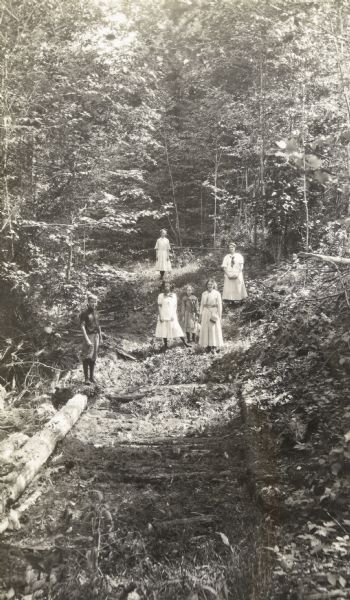 View down the first part of the path to Cathedral Woods from Barn Pond. The logs laid lengthwise and crosswise help one across the bog into the forest proper. 

From left to right is Phil Smith, Ethel Smith, then possibly Eleanor Holt. Marjorie Best is one of the other women. Caption reads: "Phil Smith, Ethel Smith, Marjorie Best."

