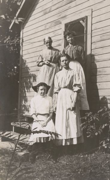 A group of three women and a girl, household employees at Island Lodge, standing in front of Green Cottage. Built in 1901, this cottage is where the cook and second girl lived. Source: Holt, Constance W. & Holt Jr., Donald R.(1968). "Place Names." This unpublished manuscript is part of Holt Family Albums collection. A thin rope, presumably a laundry line, cuts across the photograph.

Caption reads -- Top row: "Mrs. Vendt and Minnie"; Bottom row: "Viestenz, Nora Kuehl."