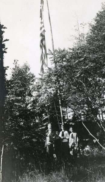 W.A. Holt and his children are standing by the flag pole, with the American flag flying. Names from left to right: Alfred Holt, W.A. Holt, Donald Holt, Jeannette Holt, and Eleanor Holt.
