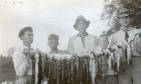 W.A. Holt (far left) and G.F. Loomis (far right) are holding up a string with the catch of the day. Standing between Holt and Loomis are: (left to right) Nathan McClure, Archibald McClure, and another boy. Caption reads: "WAH, Nathan and Arch McClure, GF Loomis."