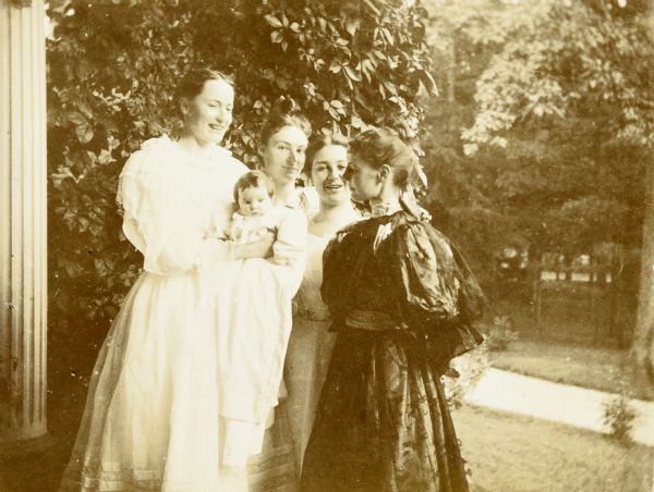 Three of Lucy Rumsey Holt bridesmaids and her mother Mary Mathilda Axtell Rumsey are adoring baby Jeannette Holt. This picture was taken on Lucy and W.A. Holt's first wedding anniversary. From left to right: Minnie May Rumsey, Jeannette Holt, {unknown}, {unknown}, and Mary Mathilda Axtell Rumsey. Caption reads: "Three of my bride's maids."