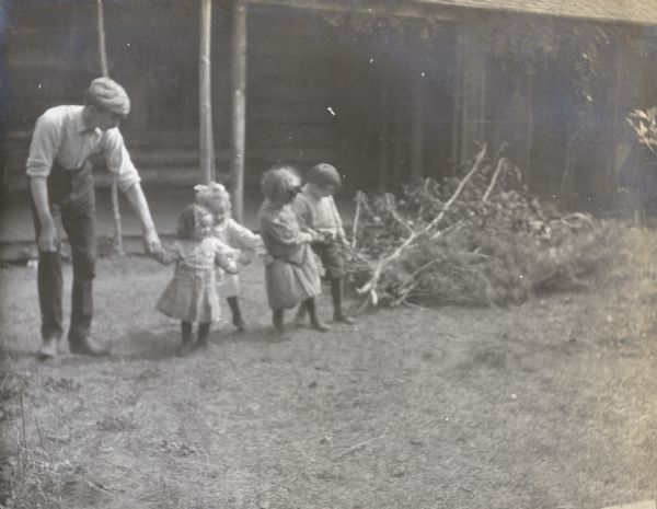 The four Holt children are helping their father haul brush. Names from left to right: W.A. Holt, Donald Holt, Eleanor Holt, Jeannette Holt, and Alfred Holt. The porch in front of Island Lodge is in the background. Caption reads: "Four-Horse Team."