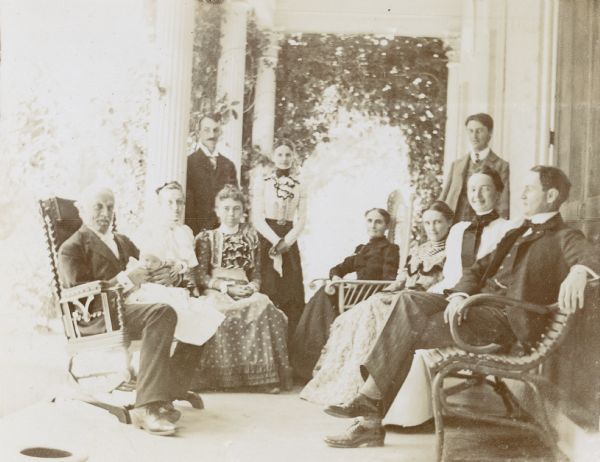 A group of Holt and Rumsey family members (3 generations) and others are gathered on the porch of The Evergreens, the Rumsey estate, to see baby Jeannette Holt. Names from left to right: Grandfather I.P. Rumsey who is holding baby Jeannette Holt, unknown, Holt Housekeeper Minnie Vendt, W.A. Holt, Lucy Rumsey Holt, Mary Mathilda Axtell Rumsey, Grant Stroh (standing), Juliet Rumsey Stroh, Minnie May Rumsey, and possibly Henry A. Rumsey.