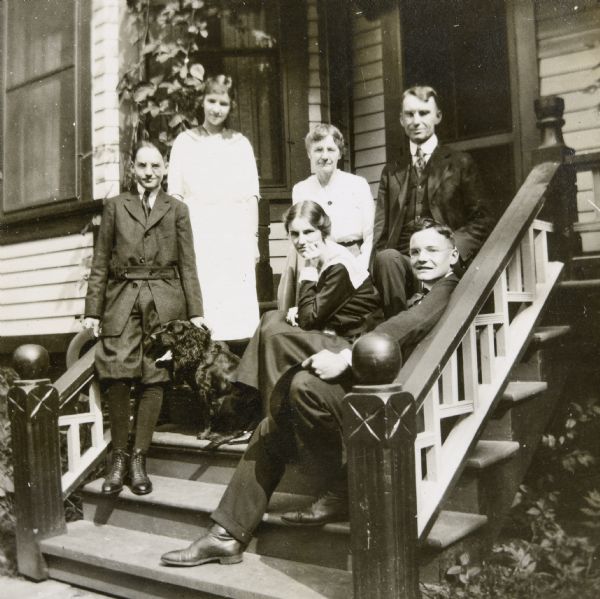 Lucy and W.A. Holt and their four children are posing on the steps of a house. Holt family members (clockwise from left to right) are: Donald Holt, Eleanor Holt, Lucy Rumsey Holt, W.A. Holt, Alfred Holt and Jeannette Holt. An English Cocker Spaniel, the family dog, is sitting next to Donald Holt.