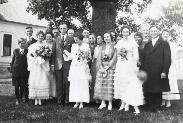 Bride Ethel M. Cecil and groom Werner W. Duecker are standing with their wedding party, family and friends.  Rev E.W. Wright officiated. The Cecil family home at 147 Washburne Ave is in the background.

Bridesmaid Jeannette Holt, to the left of the groom, is wearing an organdie dress and carrying Killarney roses. Pete {Unknown} is standing behind Jeannette Holt. Maid of honor Laura Cecil, to the right of the bride, is wearing an organdie dress with a corsage bouquet of Ophelia roses. She is holding the hand of a child. In the back row, W.A. Holt is standing to the left of the tree trunk. Father of the bride Augustine Joseph Cecil is standing to the left of W.A. Holt. 

Hubert Duecker was the best man. 

Page caption reads: "Ethel Cecil Married to Werner W. Duecker, June 1919."