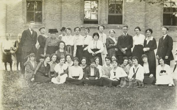 Teachers and administrators at Woodward Avenue School posing for a group portrait in front of the brick school building. Jeannette Holt is sitting in the front row, second from the left. Caption reads: "Woodward Avenue School."