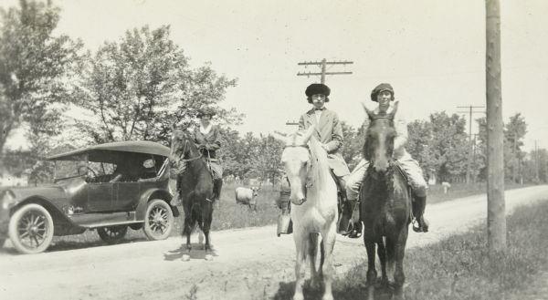 Jeannette Holt (left) and two others are horseback riding on an unpaved road. A car is parked on the other side of the road on the left, and a cow is standing in a field near trees and a telephone pole. Page caption reads: "The Howards at Kalamazoo." 


