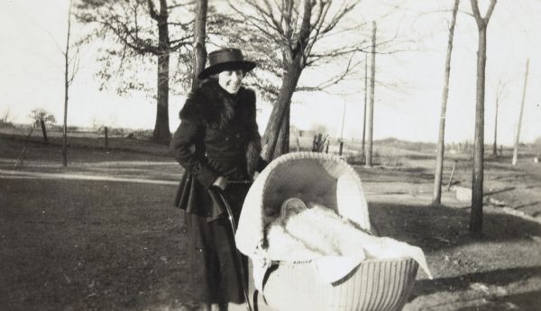 Ethel Cecil Duecker is pushing a wicker baby carriage with her son John Cecil Duecker covered with a blanket.