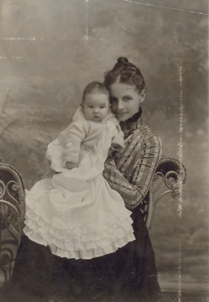 Sitting on a wicker chair, Lucy Rumsey Holt is holding her daughter Eleanor Holt who is 3 months and 10 days old. Eleanor may be wearing a christening gown. This portrait was taken in a studio with a painted backdrop. Caption reads: "Eleanor and Mother." Page caption reads: "February 10, 1901, 3 months and 10 days." 


