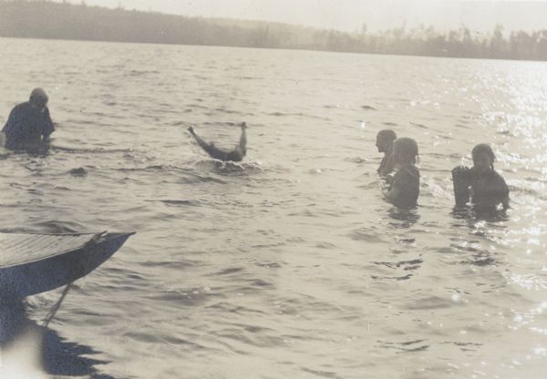 Alfred Holt is in the middle of doing a somersault from the boat into Archibald Lake. Standing in the water and watching Alfred are, from left to right: Capt. I.P. Rumsey, Jeannette Holt, Harriet Stroh, and Margaret Stroh.

Caption reads: "A Somersault from the Boat." Names in caption from left to right: "Grandfather, Alfred, J, H and M."